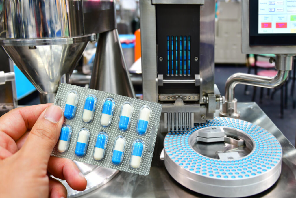 Hand holding blue capsule pack at medicine pill production line,
